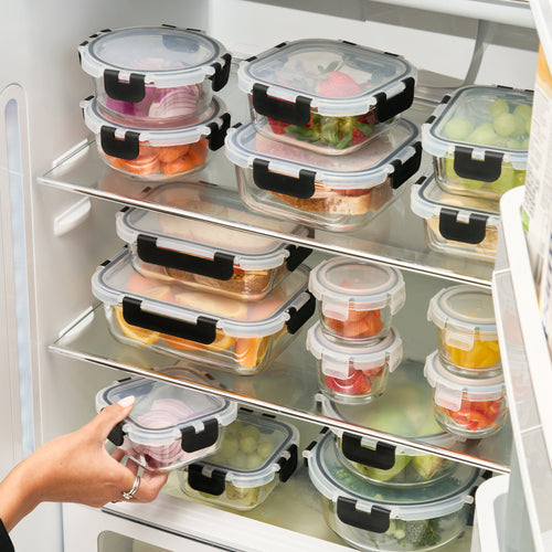 Hand reaching for one of the Storinity 32-Piece Glass Storage Containers, filled with food and stacked on fridge shelves
