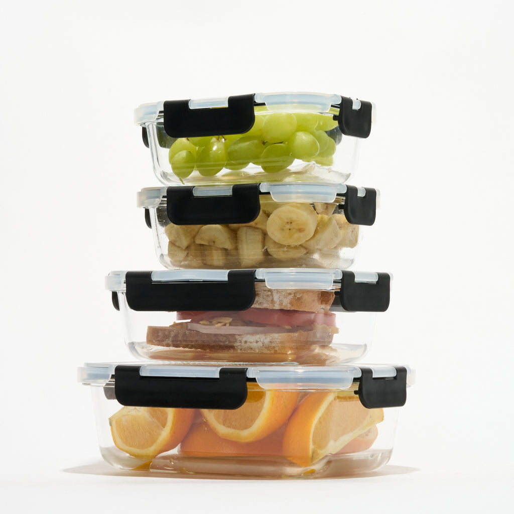 Stack of four rectangular Storinity glass containers filled with grapes, banana, a sandwich and orange slices