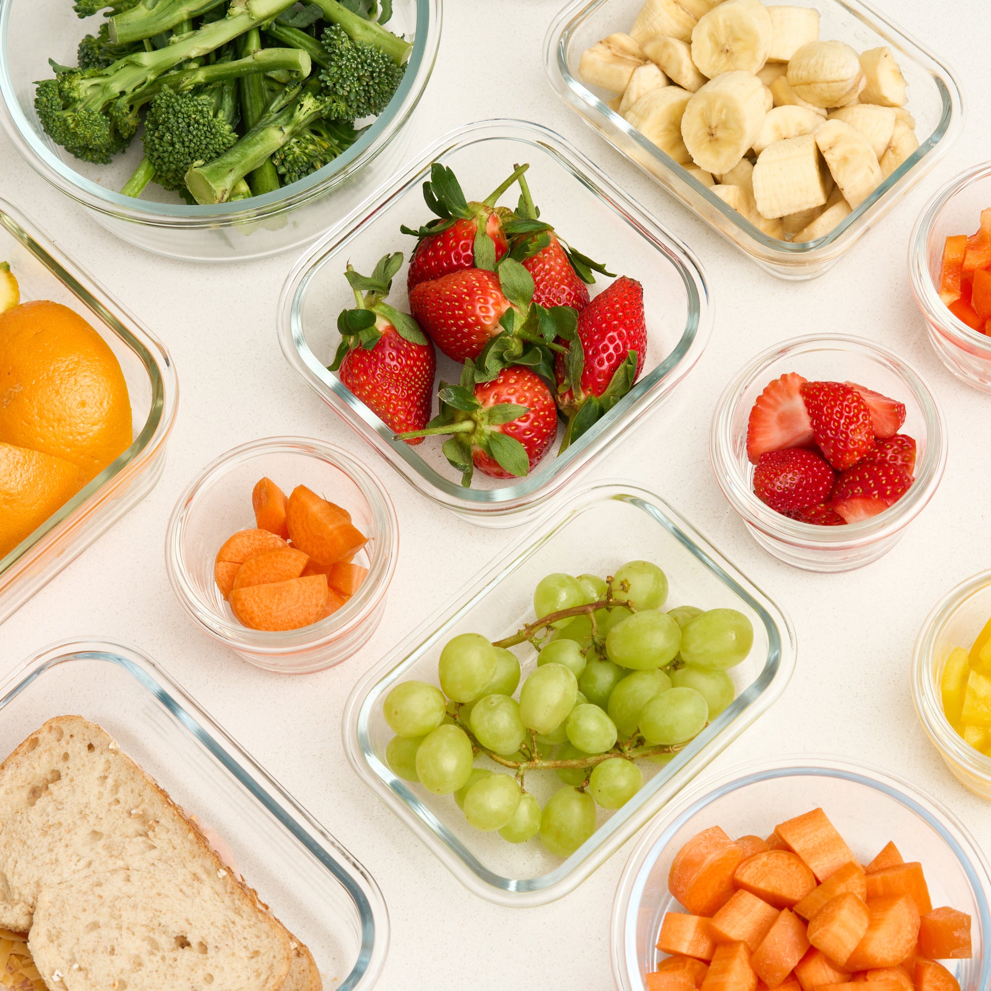 Overhead view of open Storinity glass containers filled with broccoli, strawberries, grapes, carrots and bread