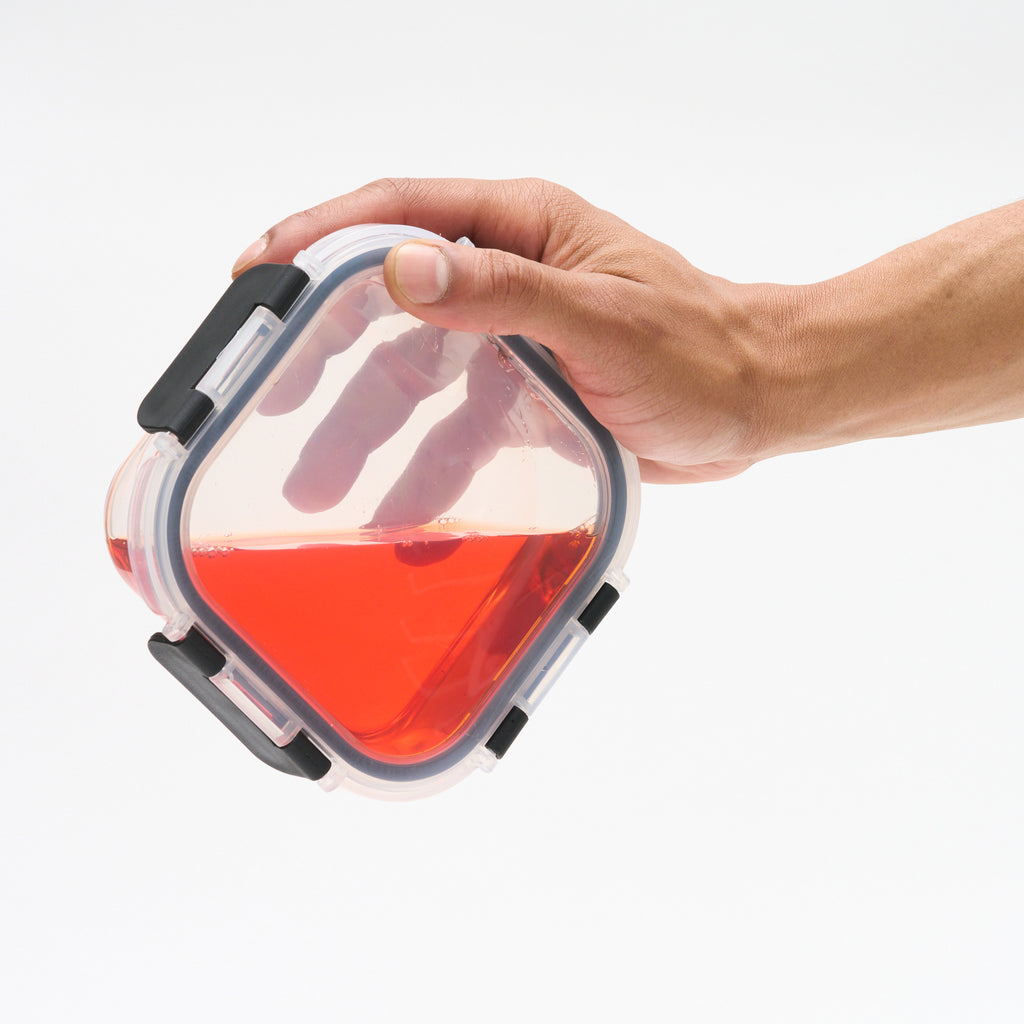 Hand tilting a Storinity glass storage container filled with red liquid to demonstrate the leak-proof seal