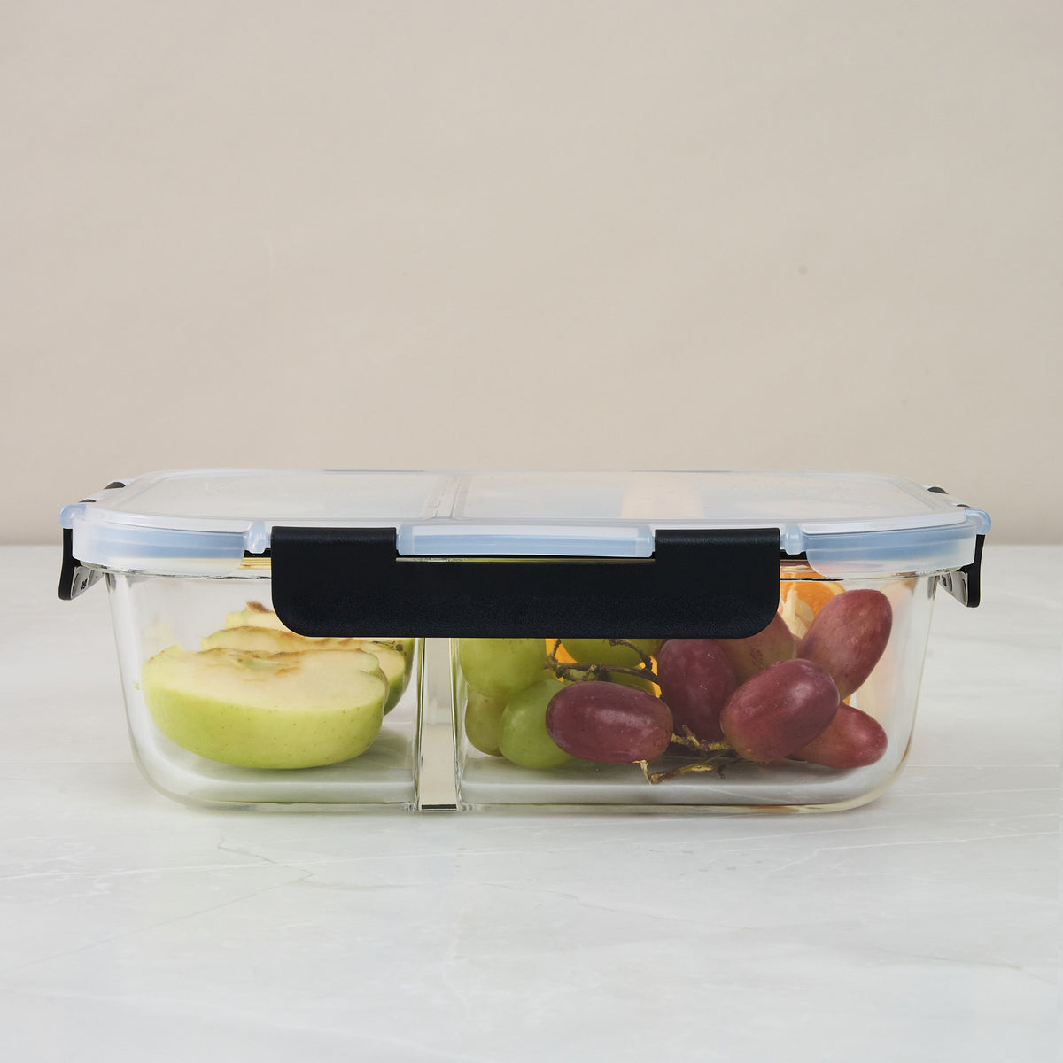 Closed Storinity divided glass container filled with apple slices and grapes, front view