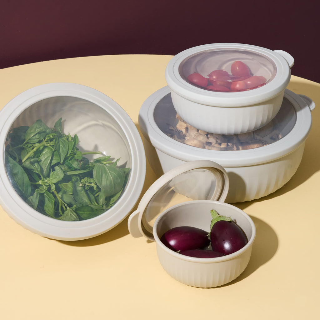 Storinity nesting bowls filled with basil, mushrooms, cherry tomatoes and baby eggplants, styled on a yellow surface