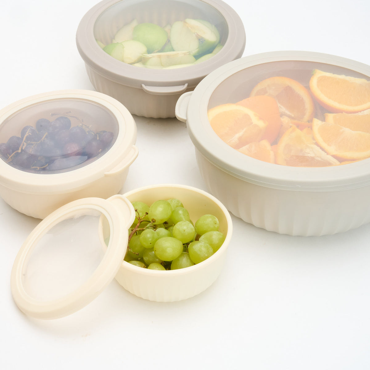 Storinity nesting bowls with lids on filled with apple, black grapes and orange, with one open bowl of green grapes in front