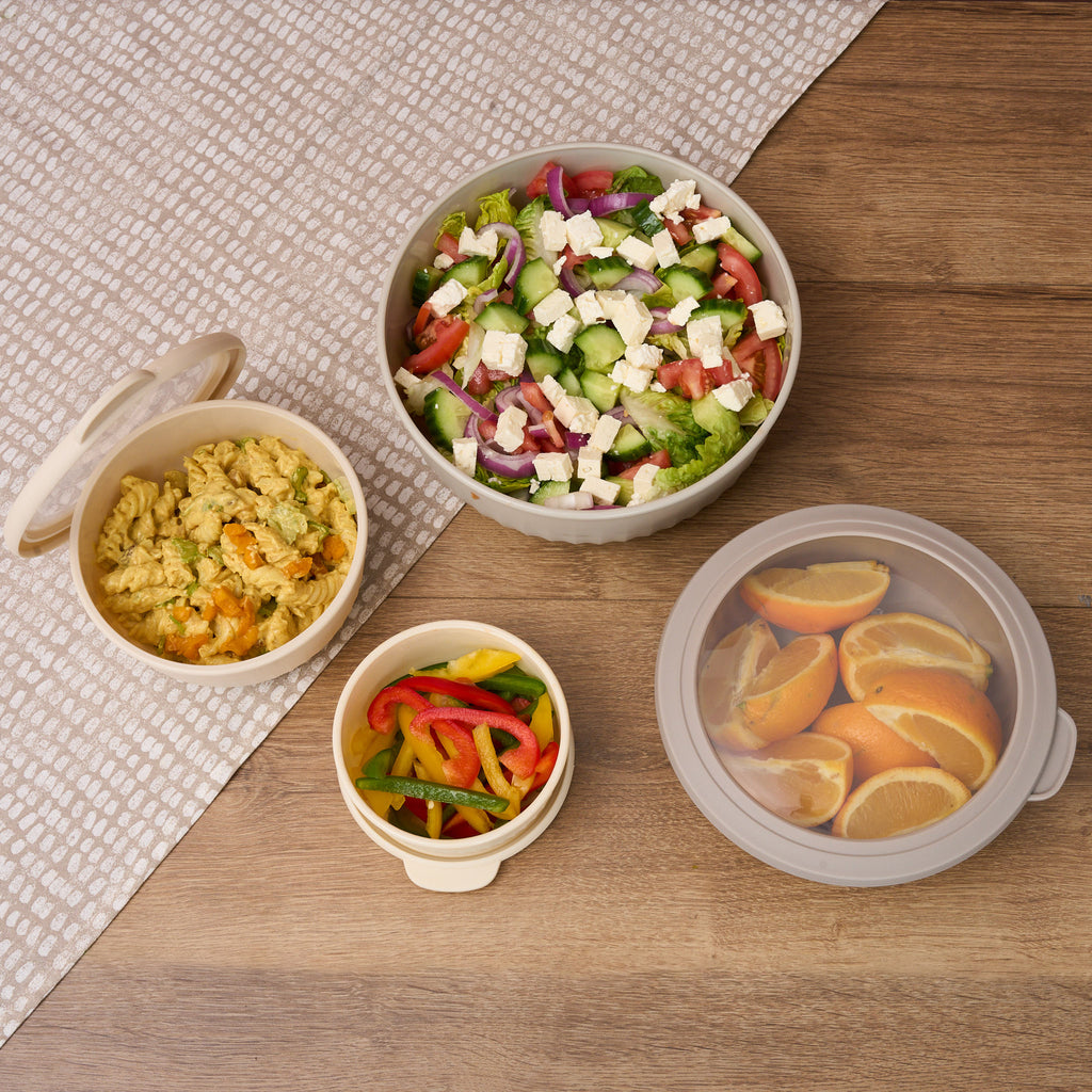 Overhead view of Storinity nesting bowls filled with Greek salad, pasta salad, peppers and orange segments on a wooden table