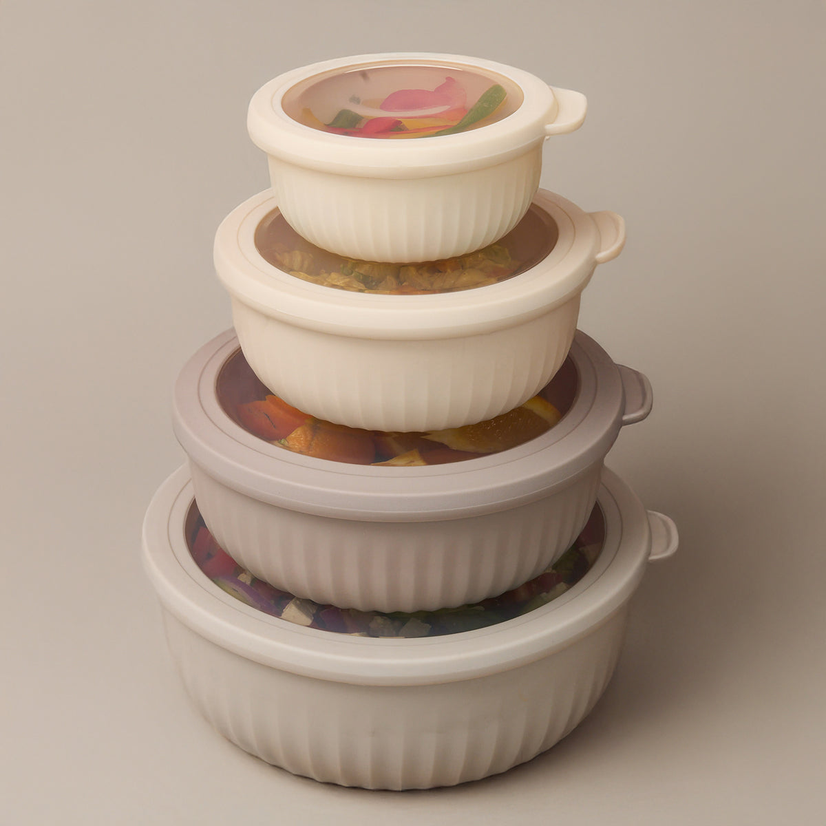 The four Storinity nesting bowls stacked with lids on, filled with colourful ingredients, on a beige background