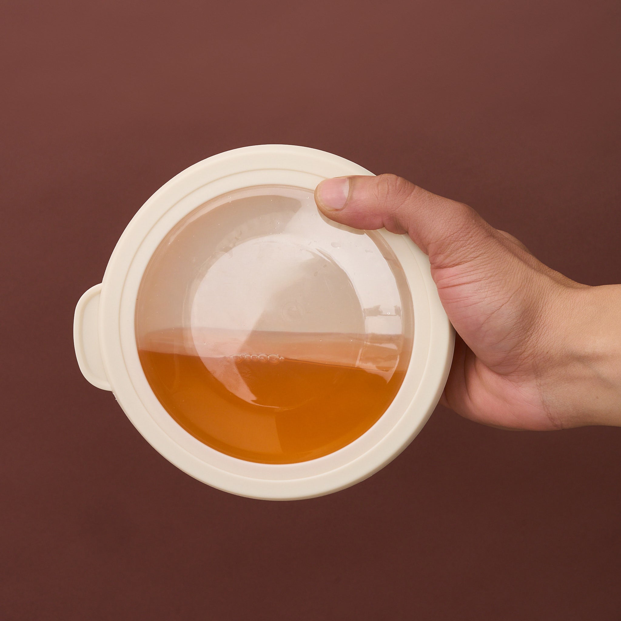 Hand tilting a sealed Storinity nesting bowl filled with orange liquid to demonstrate the leak-proof seal