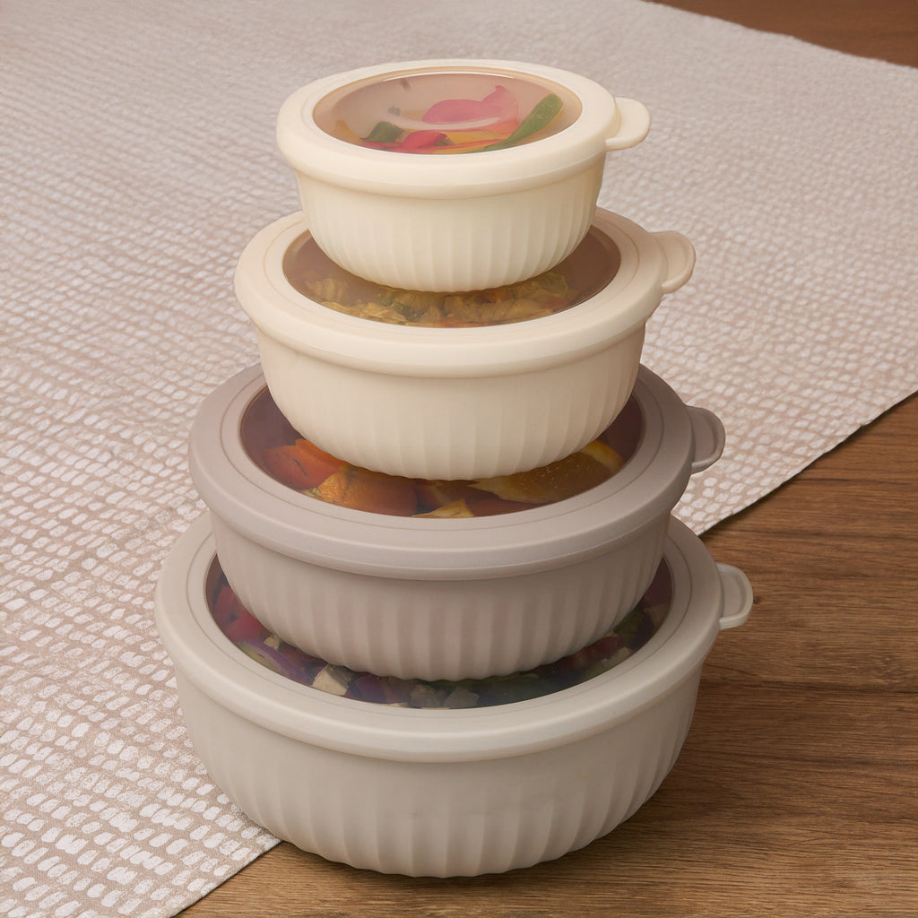 The four Storinity nesting bowls stacked with lids on, filled with colourful ingredients, on a wooden table with cloth