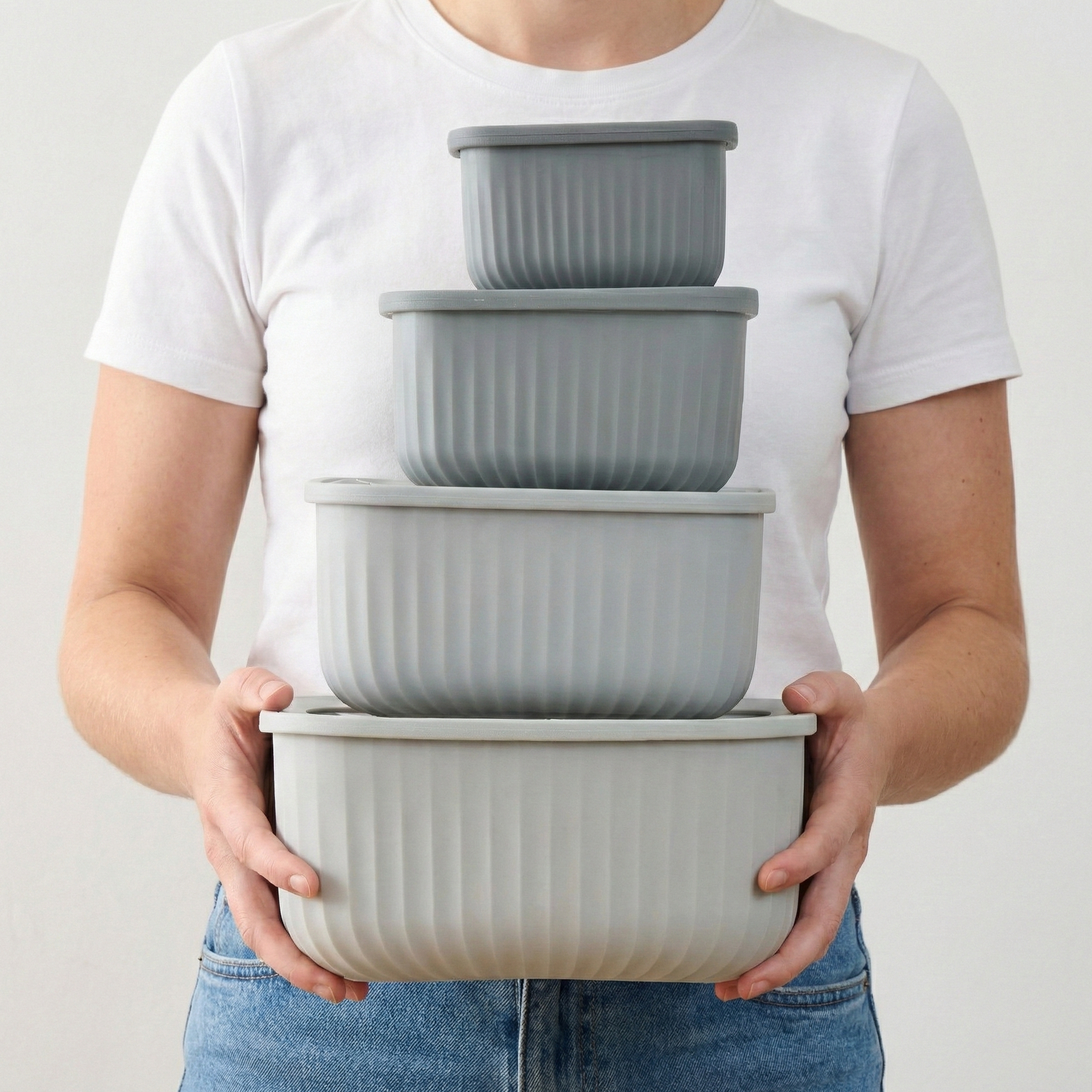 Person in a white t-shirt holding the stacked set of four empty grey Storinity rectangular nesting bowls