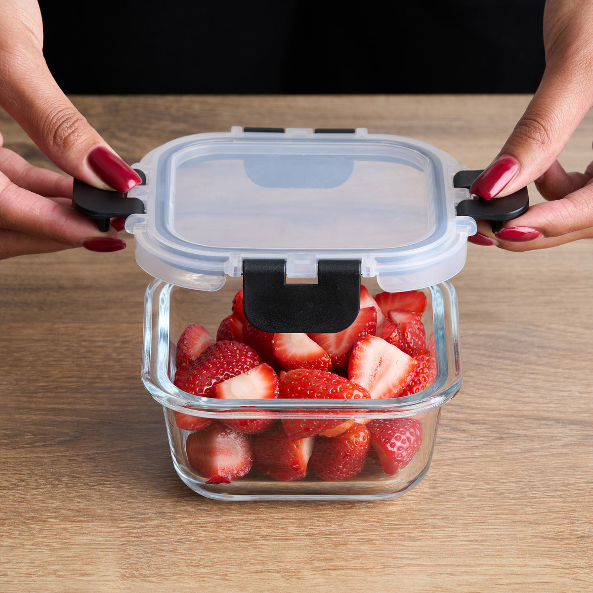 Hands closing the air tight locking clips on a glass container of strawberries