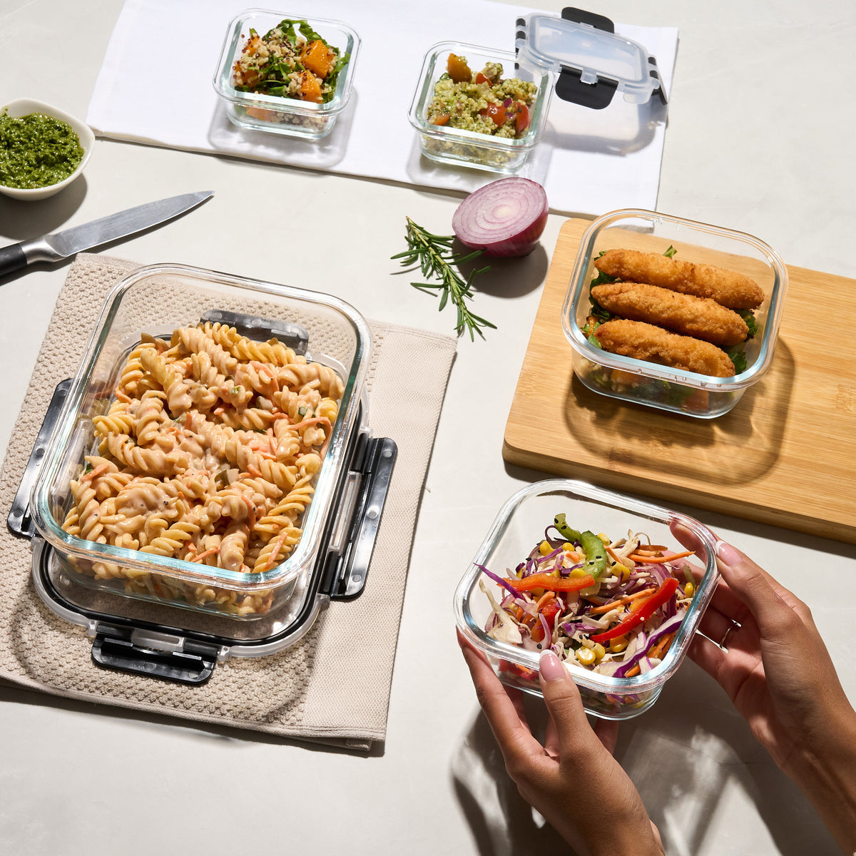 Storinity glass containers filled with grain salad, pesto rice salad, pasta salad, crumbed fish and coleslaw on a table