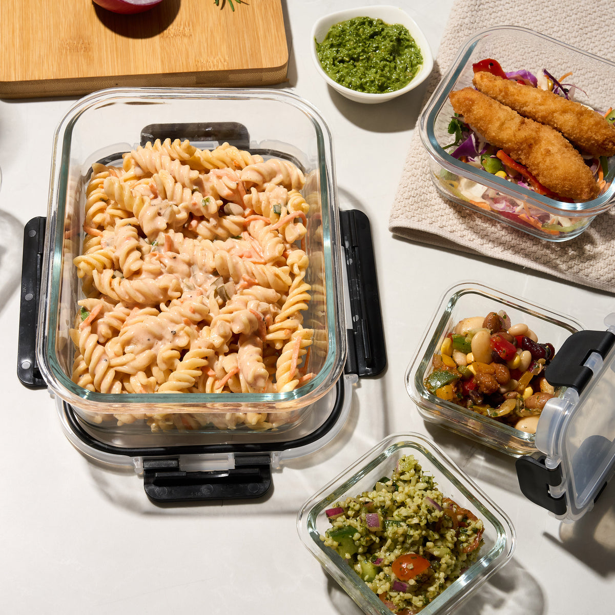 Overhead view of Storinity glass containers filled with pasta salad, crumbed fish, bean salad and pesto rice salad