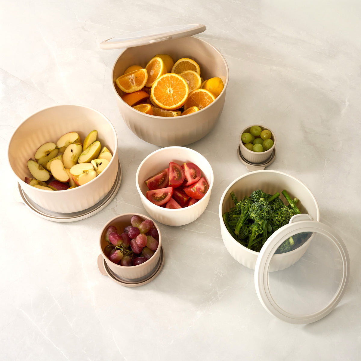 Overhead view of Storinity nesting bowls filled with orange and lemon slices, apple, grapes, tomatoes and broccoli