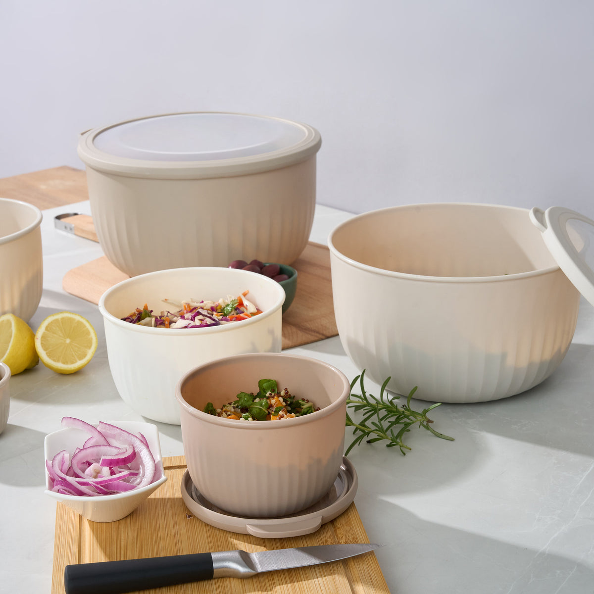 Storinity nesting bowls with coleslaw and quinoa salad, styled with lemon, red onion, rosemary and a knife on a cutting board