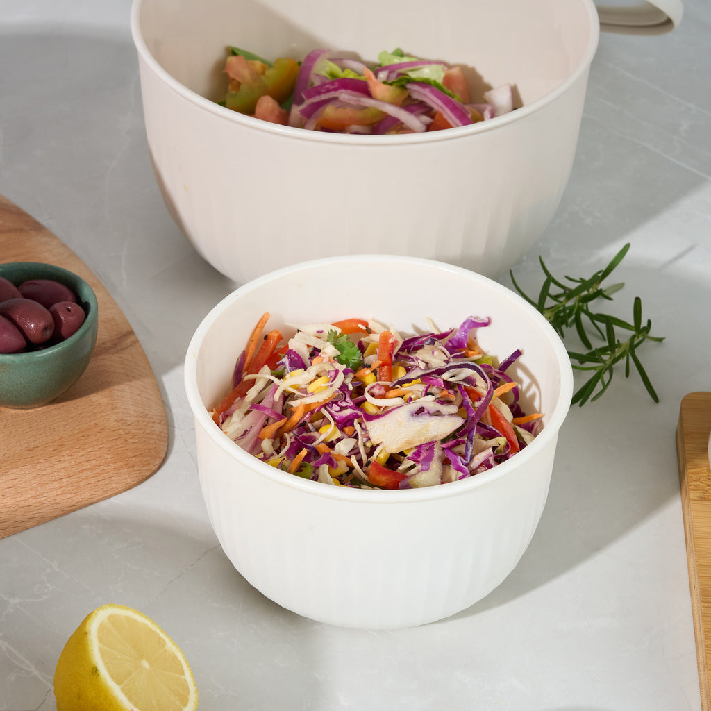 Close-up of Storinity nesting bowls filled with a mixed salad and coleslaw, with olives, lemon and rosemary