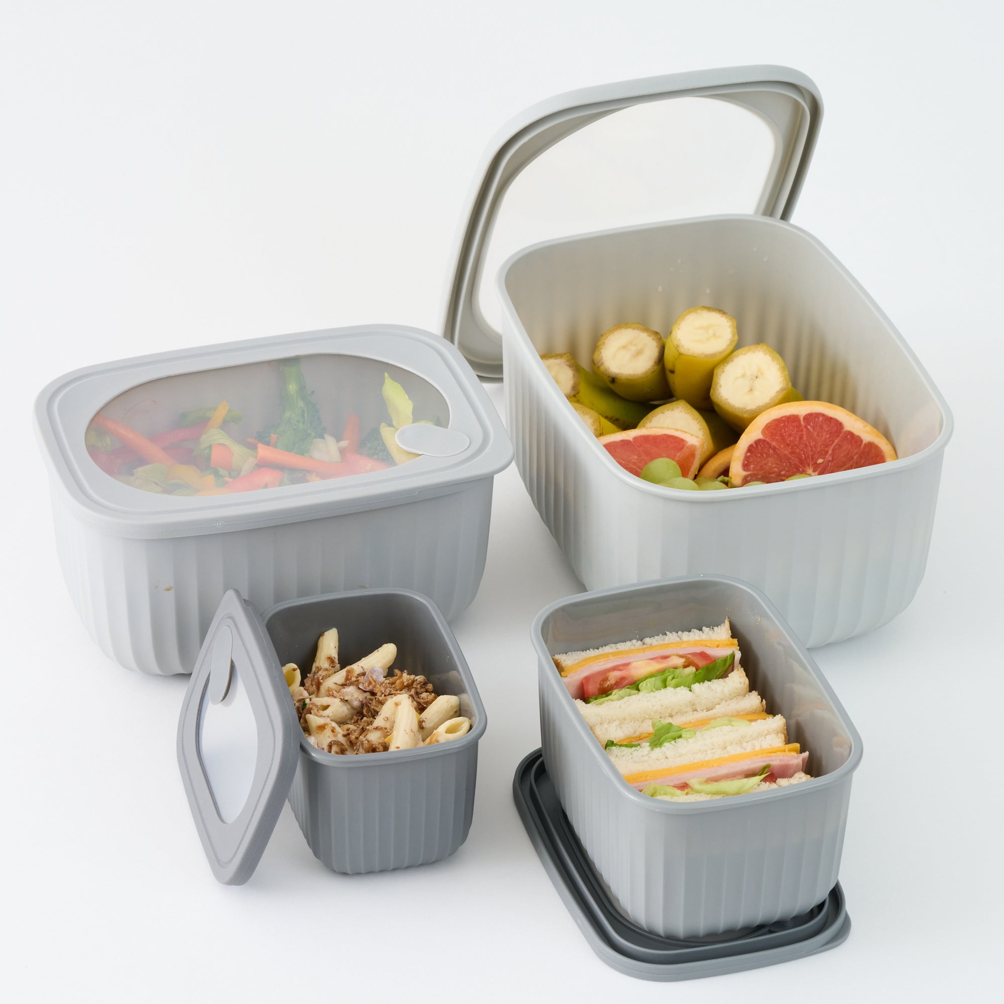 Grey Storinity rectangular nesting bowls filled with vegetables, fruit, pasta and sandwiches, some with lids open