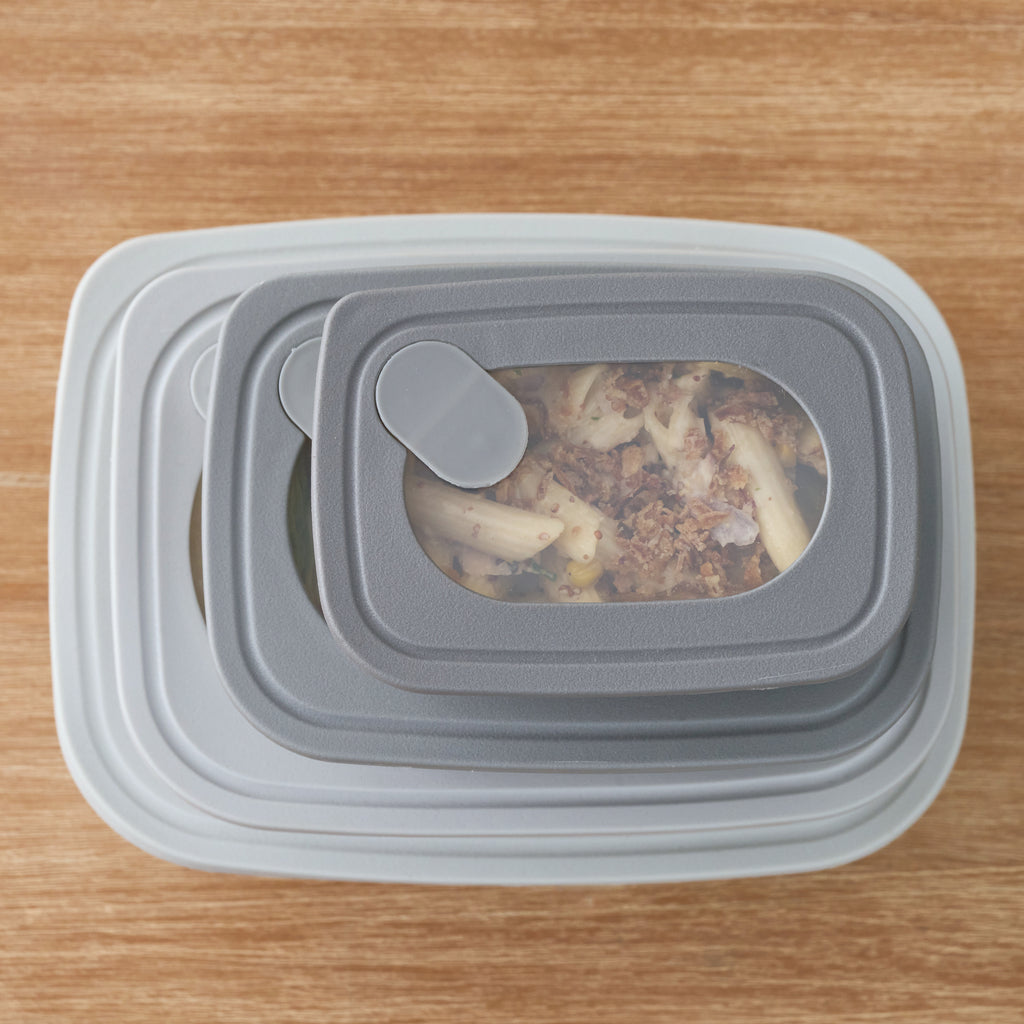 Overhead view of stacked grey Storinity rectangular nesting bowls with pasta visible through the vented lid, on a wooden table