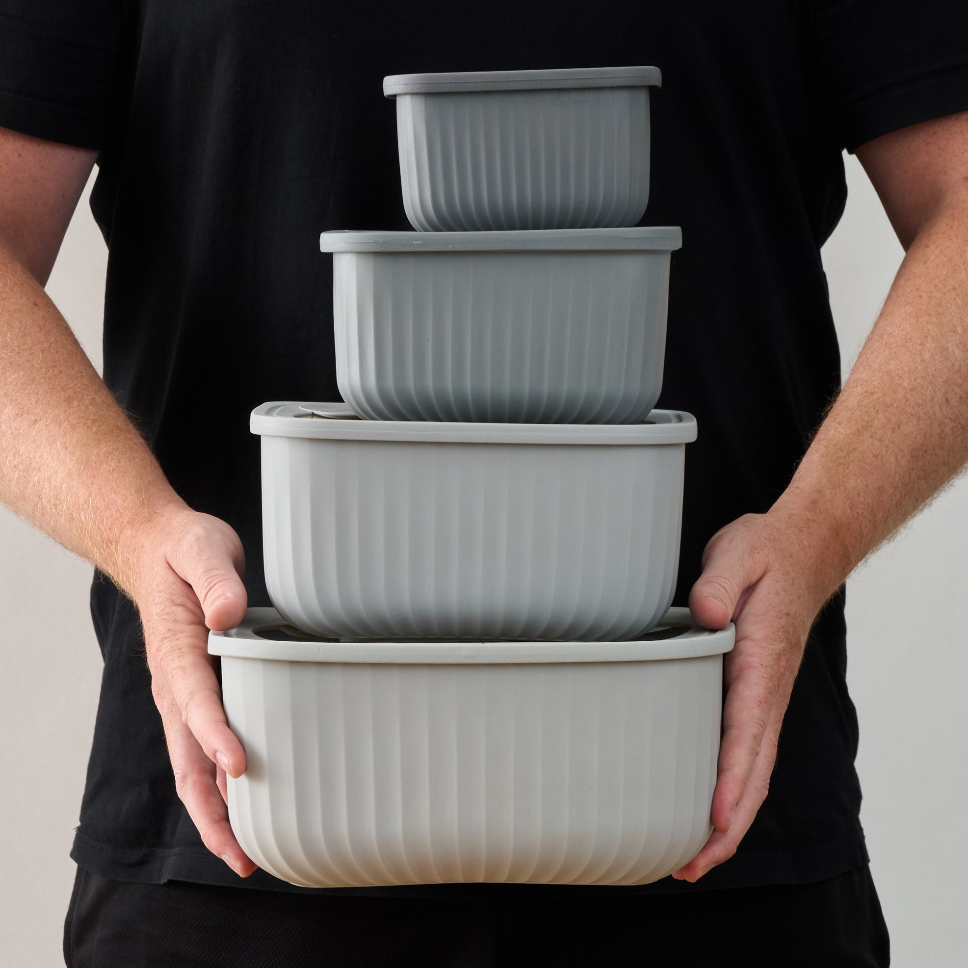 Person holding the stacked set of four empty grey Storinity rectangular nesting bowls with both hands