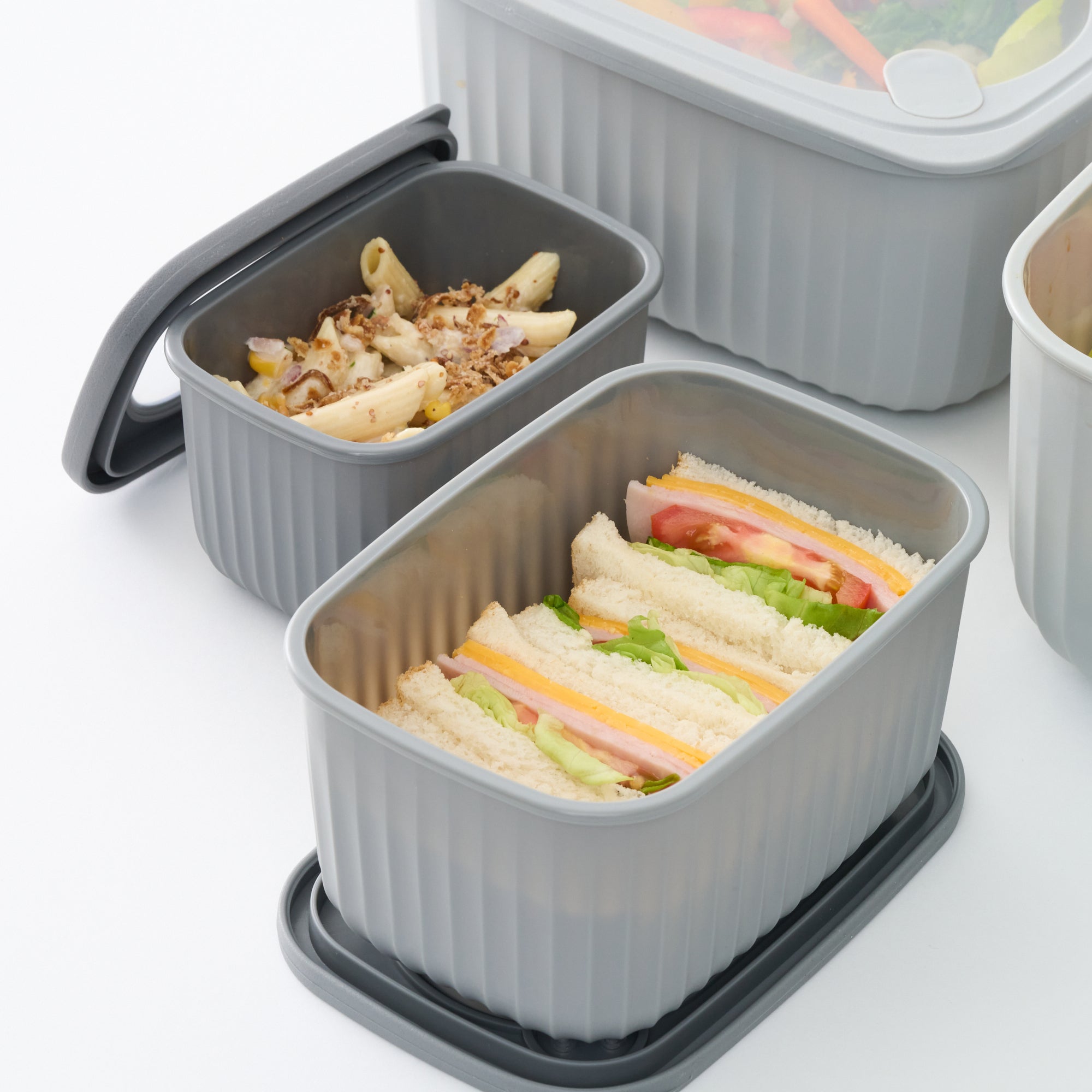 Close-up of open grey Storinity rectangular bowls filled with pasta salad and sandwiches