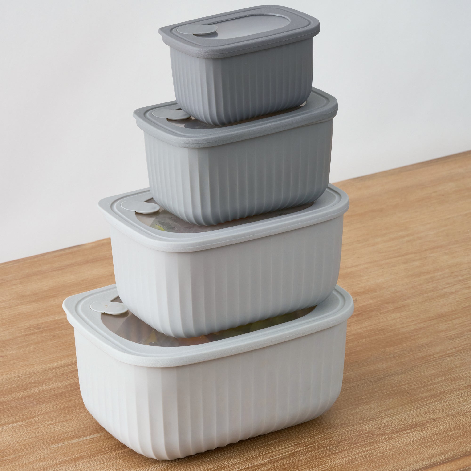 The four grey Storinity rectangular nesting bowls stacked at an angle on a wooden table, some containing food
