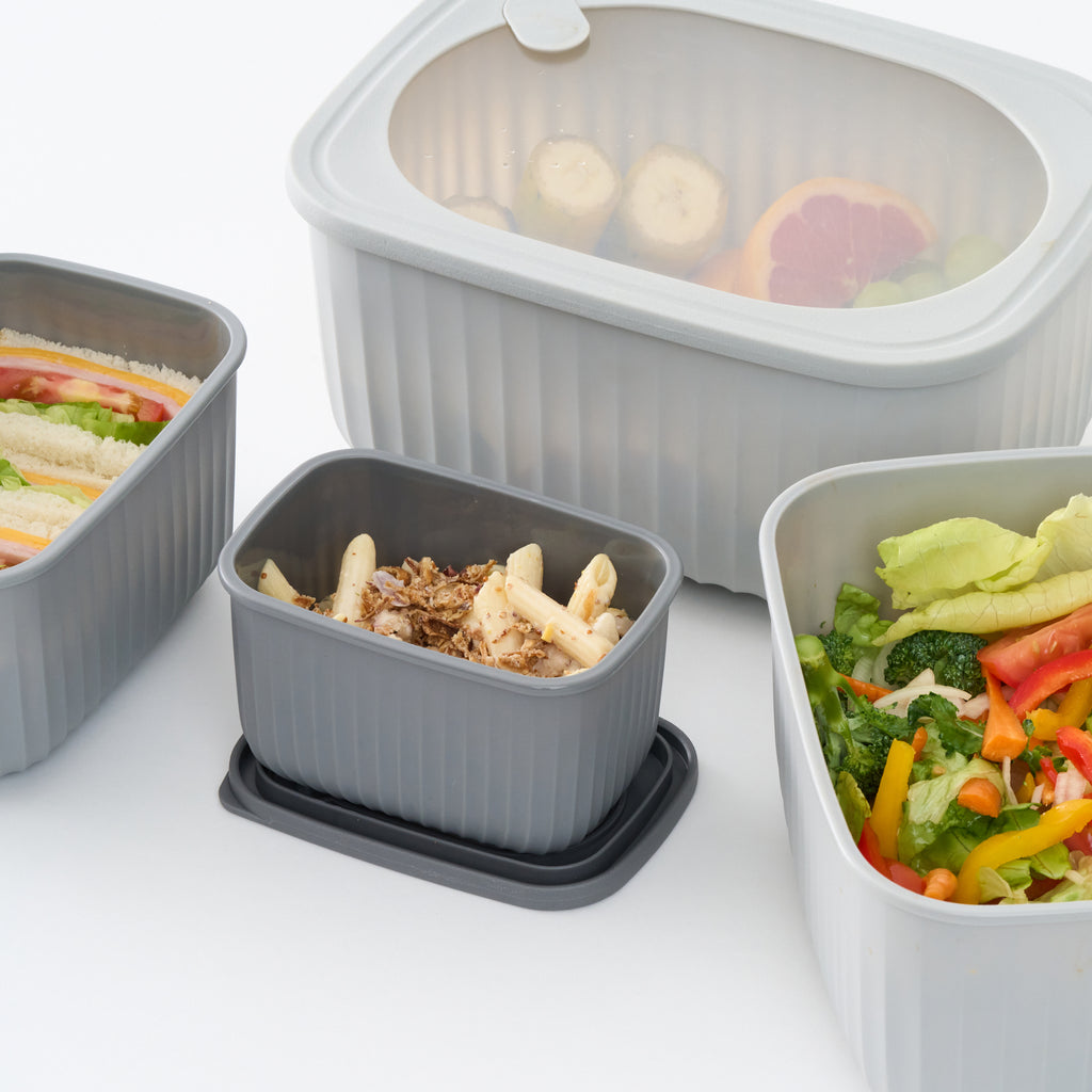 Close-up of four grey Storinity rectangular bowls filled with sandwiches, fruit, pasta and salad